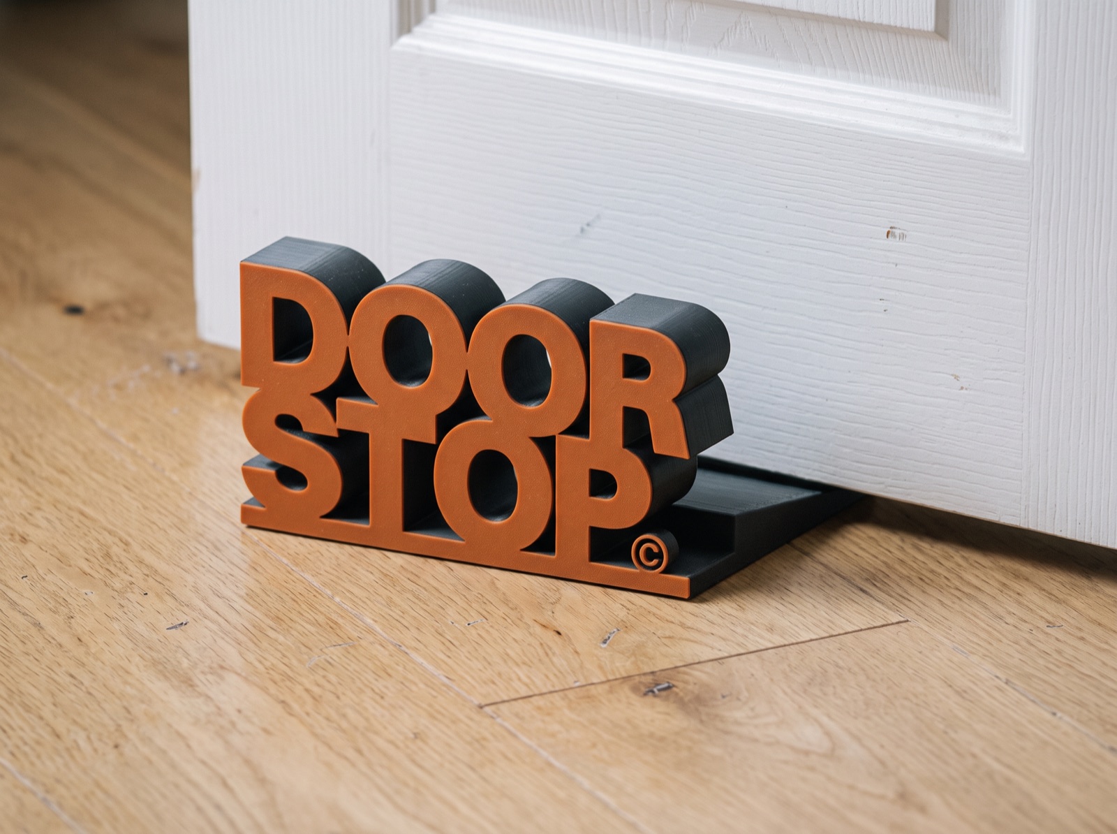 DOOR STOP in orange and charcoal wedged under a white panel door on an oak floor