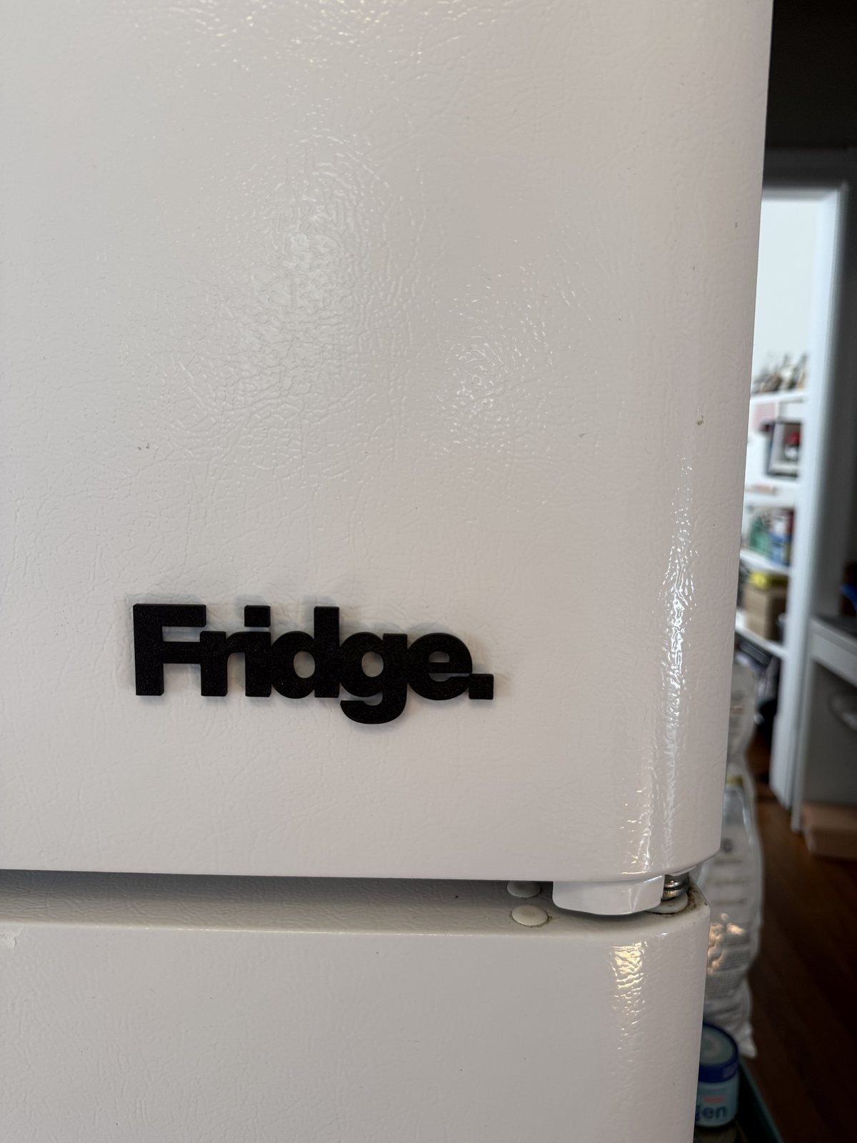 The black Fridge. magnet on the door of a white fridge, low on the door near the hinge