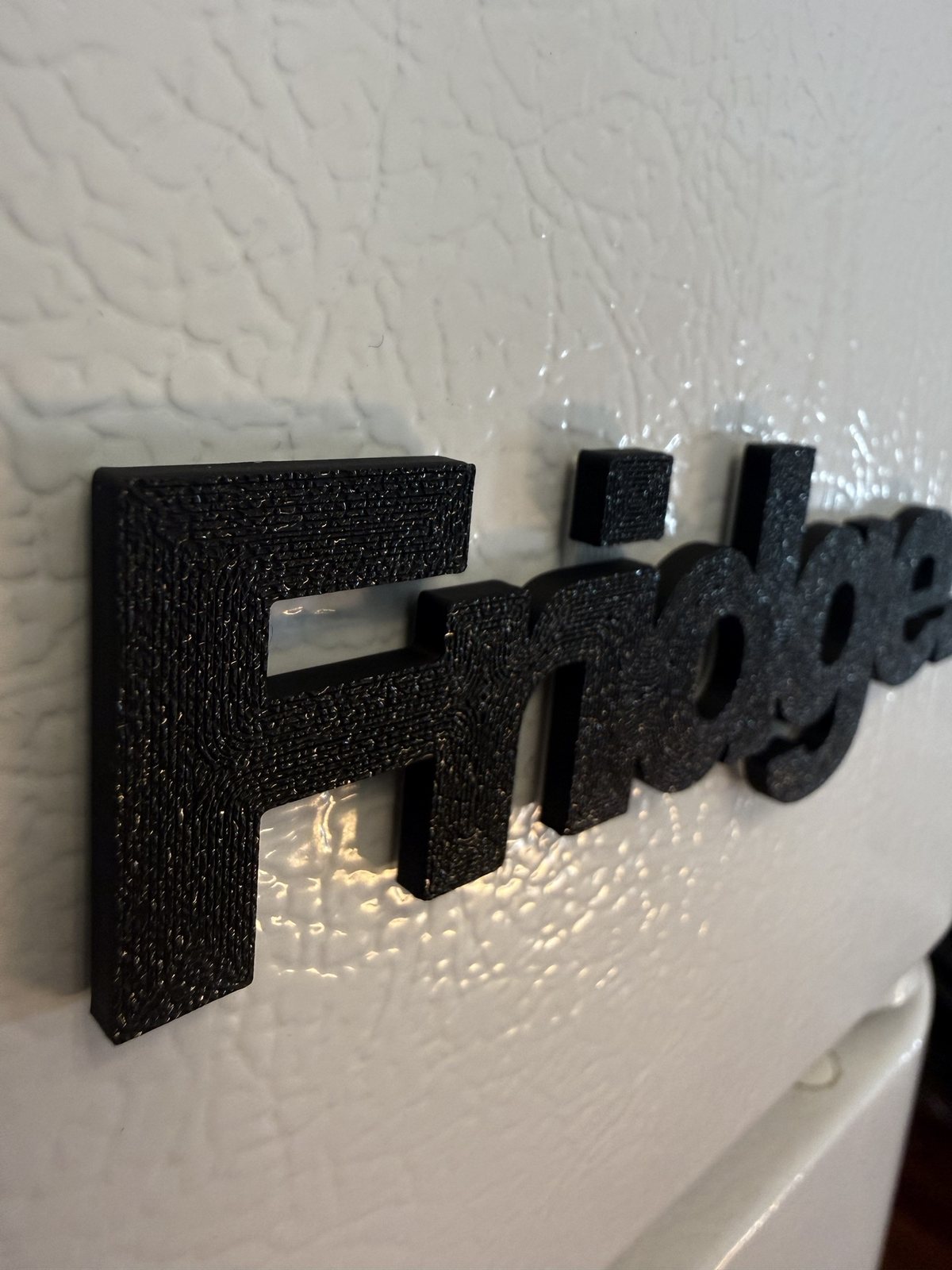 Close up from the side: the F, r and the square dot of the i, the textured black face standing about 4 mm off the fridge